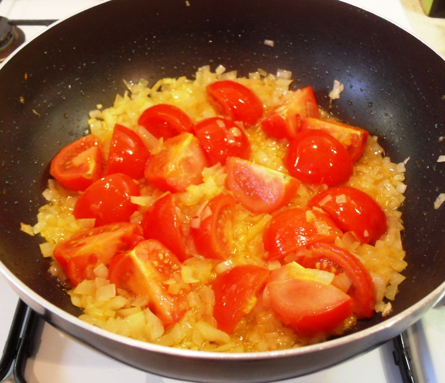 Tomatoes and onions softening in oil in a pan.