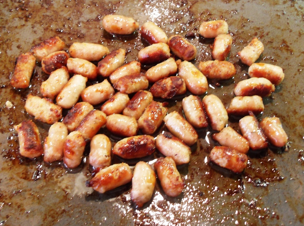 Cooked chipolatas on a baking tray.