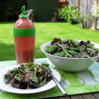 Raspberry Vinaigrette in an Oxo Goodgrips Salad Shaker next to a bowl of salad and a plate of salad which has some dressing poured on.