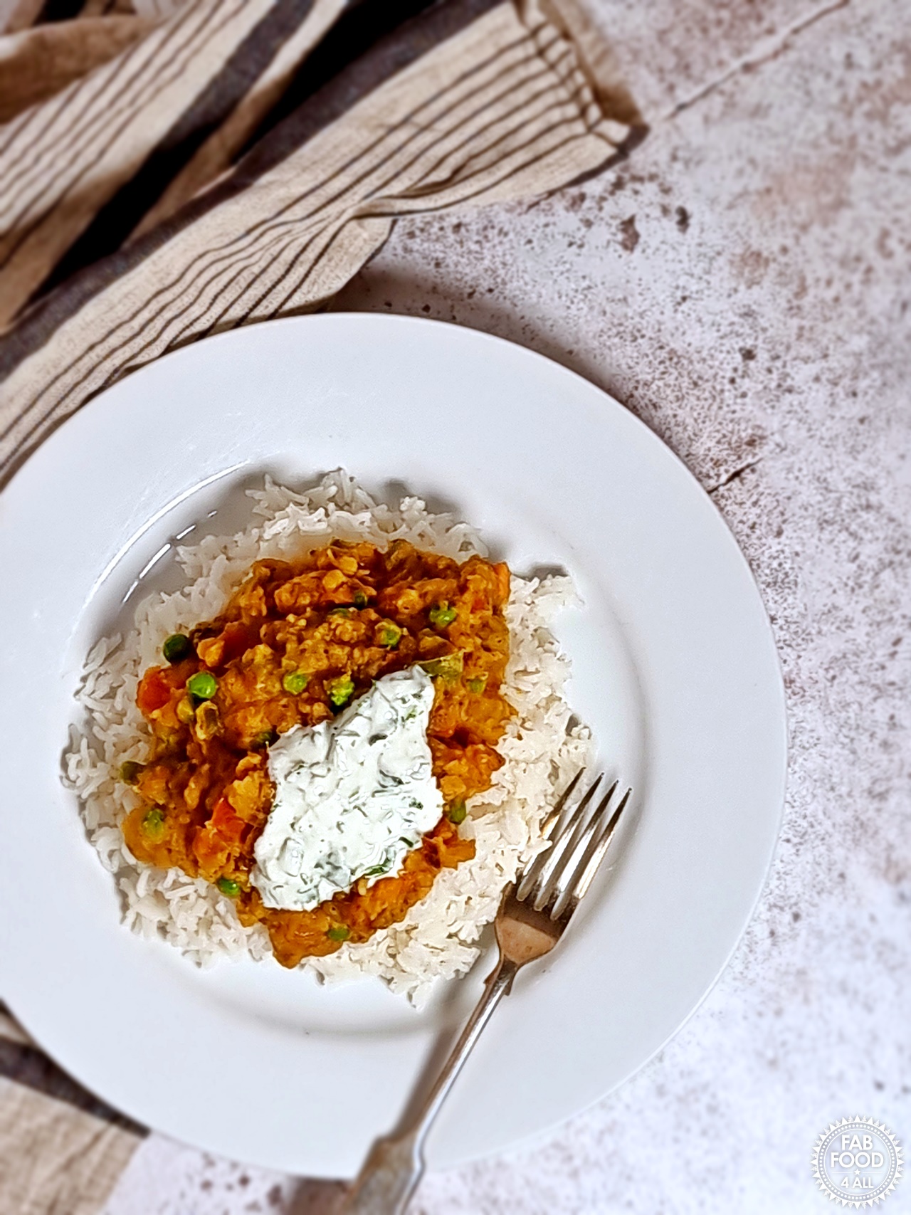 Overhead shot of Vegetable Dhal Curry with rice & garnished with coriander yogurt dressing.