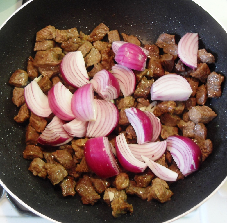 Chopped red onions added to cooked beef in a pan.