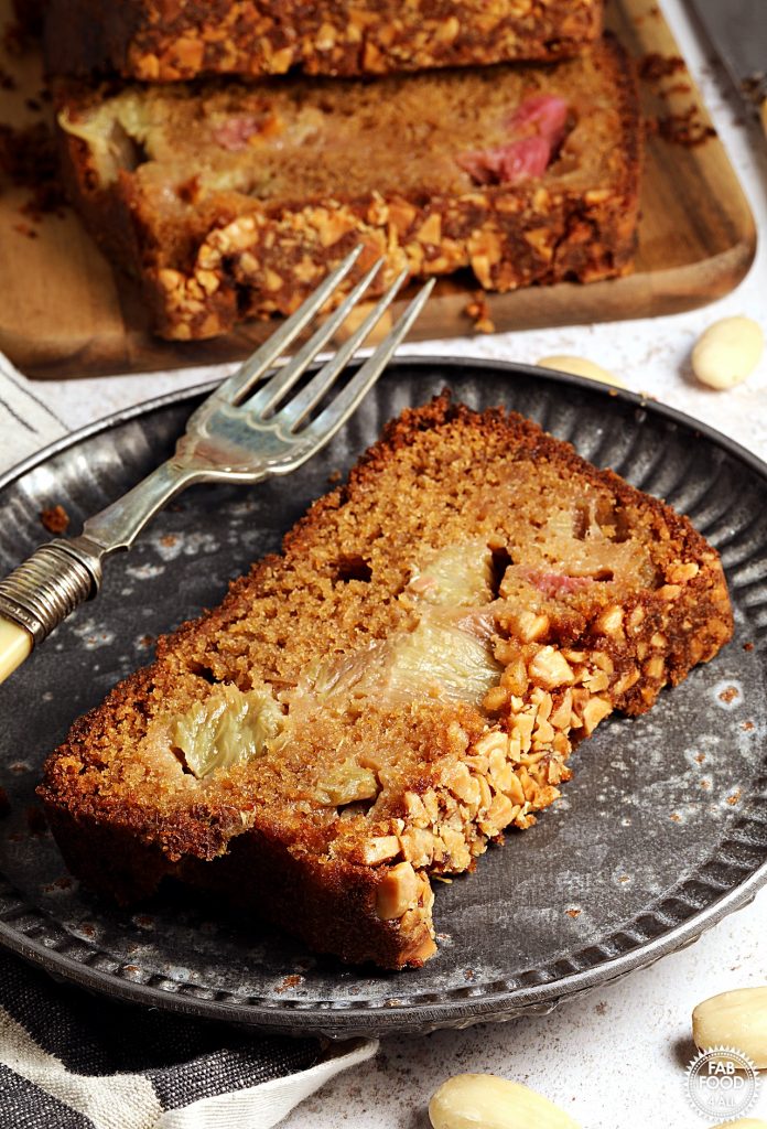 Slice of Rhubarb & Ginger Cake on a metal plate with cake in background.