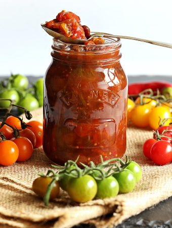 Mixed Tomato Chutney in a jar surrounded by cherry tomatoes in various colours.