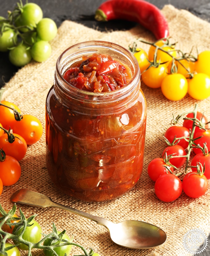 A jar of Mixed Tomato Chutney surrounded by green, red, yellow & orange cherry tomatoes.