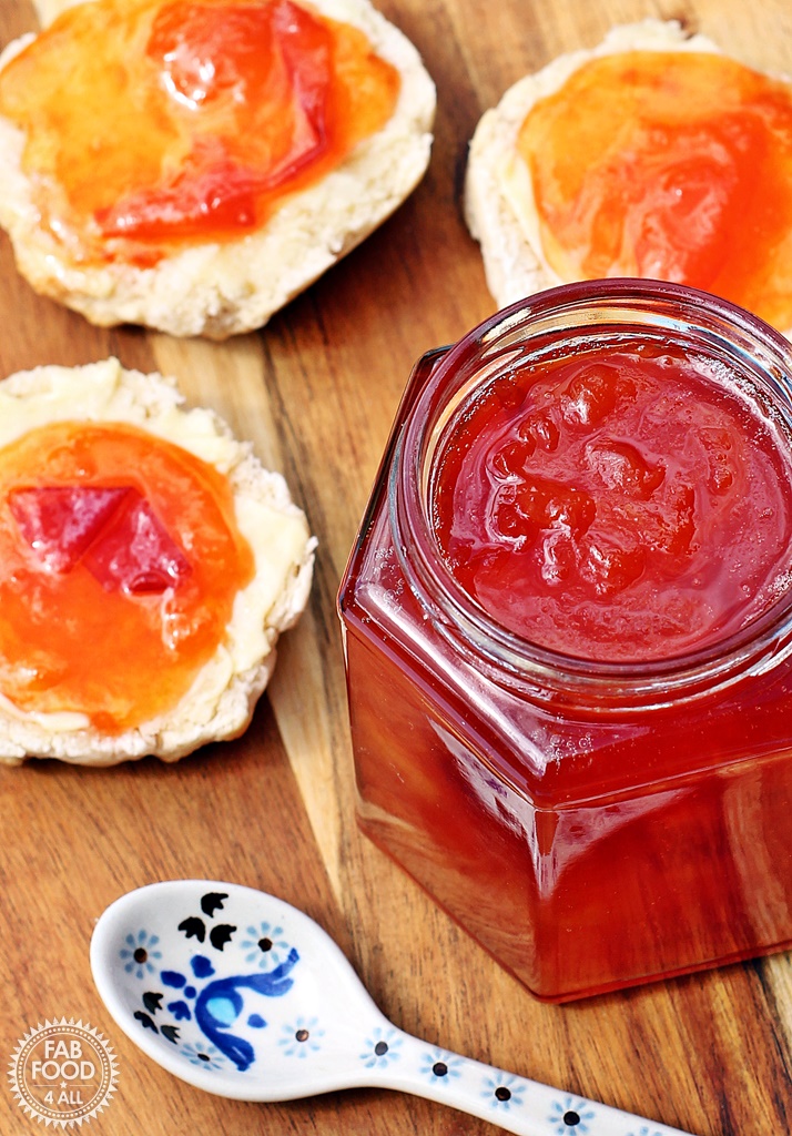 Jar of Peach & Apricot Jam with a spoon and scones on a wooden board.