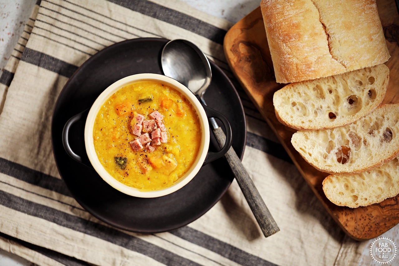 Aerial shot of Lentil & Ham Soup with bread on a board.