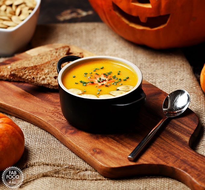 Curried Pumpkin Soup in a bowl on a board in front of pumpkins.
