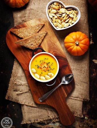 Curried Pumpkin Soup on a board with toast and toasted pumpkin seeds in a bowl.