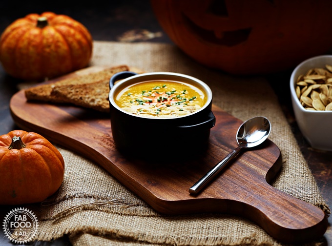 Curried Pumpkin Soup in a bowl on a board in front of pumpkins.