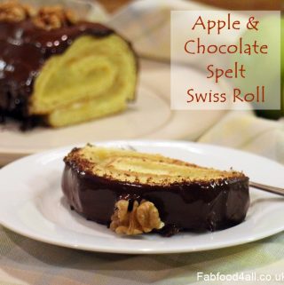 Apple & Chocolate Swiss Roll slice on a plate with main cake in background.