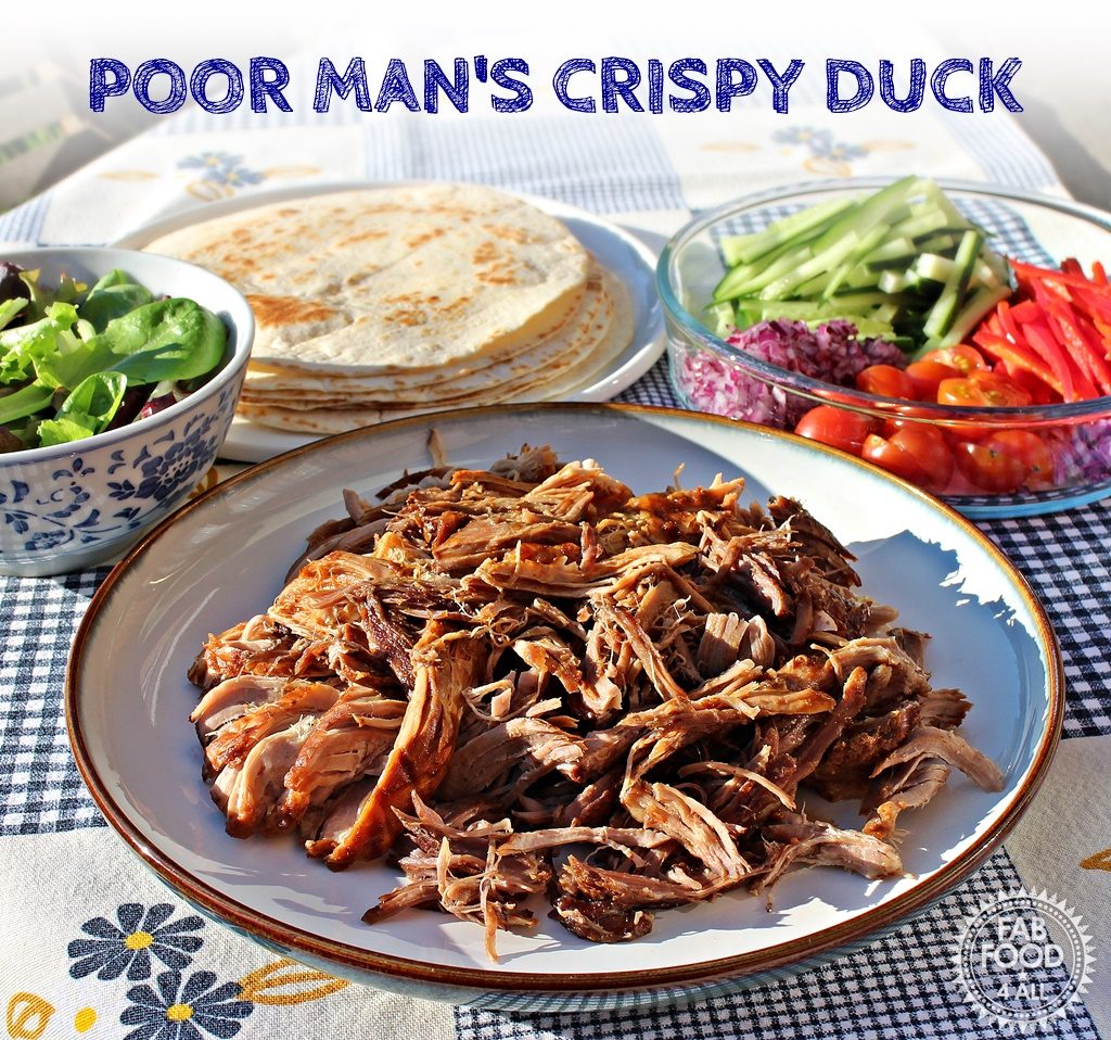 Plate of Poor Man's Crispy Duck that is Pulled Hoisin Pork along with a bowl of salad leaves, dish of chopped onion red pepper, cherry tomatoes and cucumber strips plus a plate of flour tortillas.