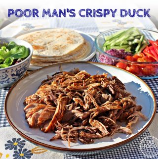 Plate of Poor Man's Crispy Duck that is Pulled Hoisin Pork along with a bowl of salad leaves, dish of chopped onion red pepper, cherry tomatoes and cucumber strips plus a plate of flour tortillas.