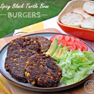 Spicy Black Turtle Bean Burgers,on a plate with salad and buns in basket in background.