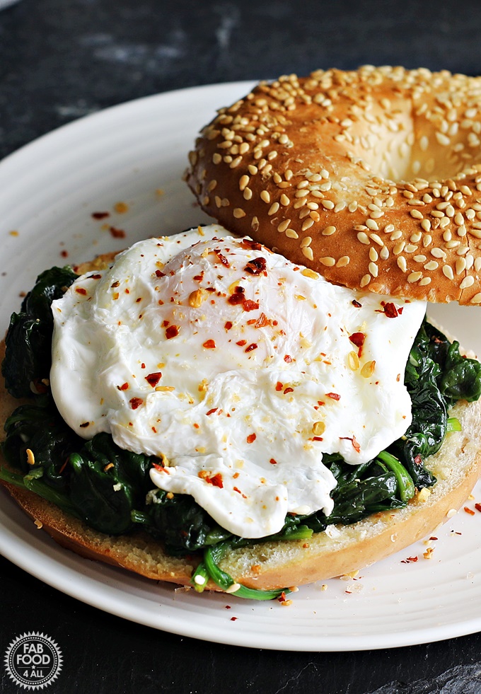 Quick Poached Egg & Garlic Spinach Bagel served on a white plate on a slate.