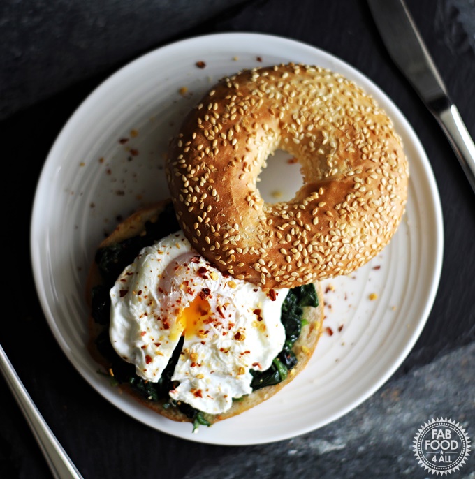 Quick Poached Egg & Garlic Spinach Bagel served on a white plate on a slate.
