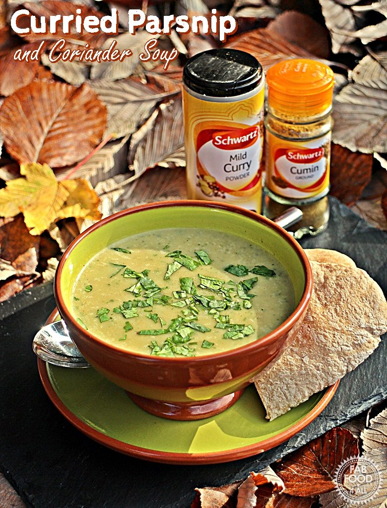 Curried Parsnip and Coriander Soup in a bowl with pitta on a plate on a green slate surrounded by autumn leaves with pot of curry powder and jar of cumin in background.