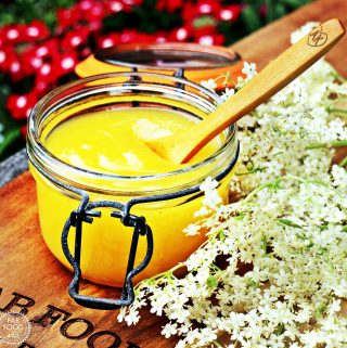 Easy Lemon & Elderflower Curd in a Kilner jar with wooden teaspoon and elderflowers.