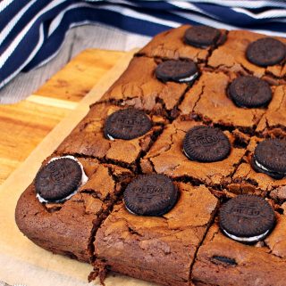 Oreo Brownies cut up on a wooden board with tea towel in background.