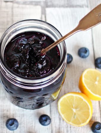 Simple Blueberry Jam in a jar with cut lemon & blueberries surrounding.