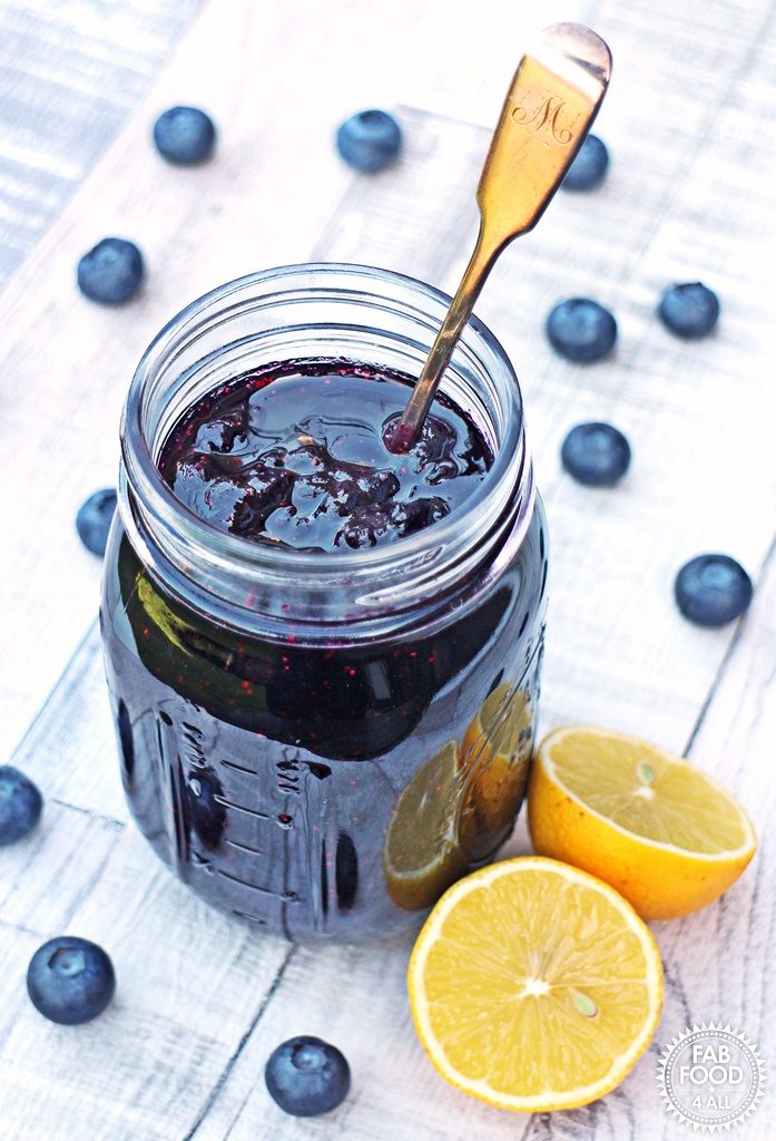 Simple Blueberry Jam in a jar with cut lemon & blueberries surrounding.