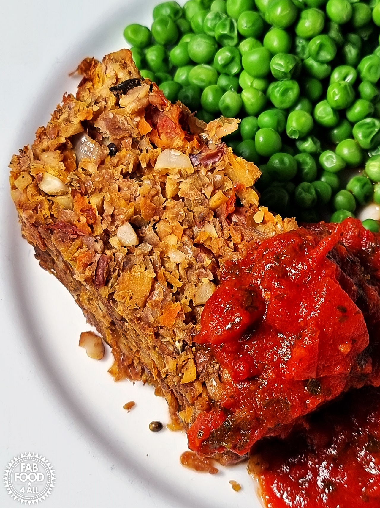 Nut Roast on a plate with peas a chilli sauce.