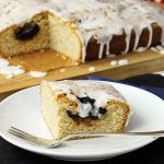 Spiced Prune Traybake slice on a plate with a cake fork and the rest of the traybake in the background on a wooden board.