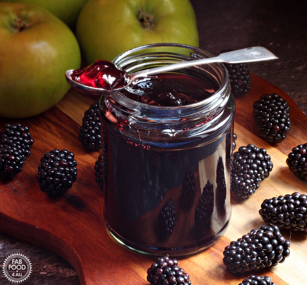 Jar of Easy Blackberry & Apple Jelly on a board with Bramley apples and blackberries.