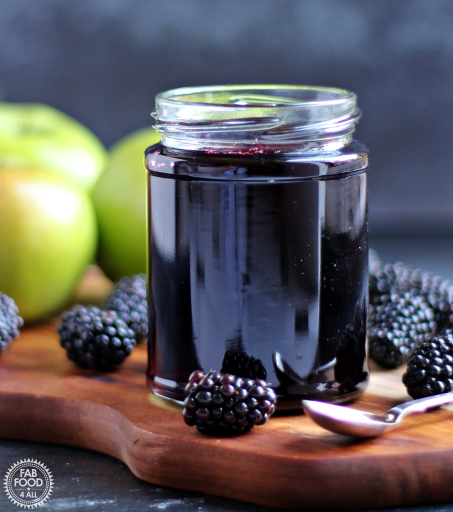 Jar of Easy Blackberry & Apple Jelly on a board with Bramley apples and blackberries.