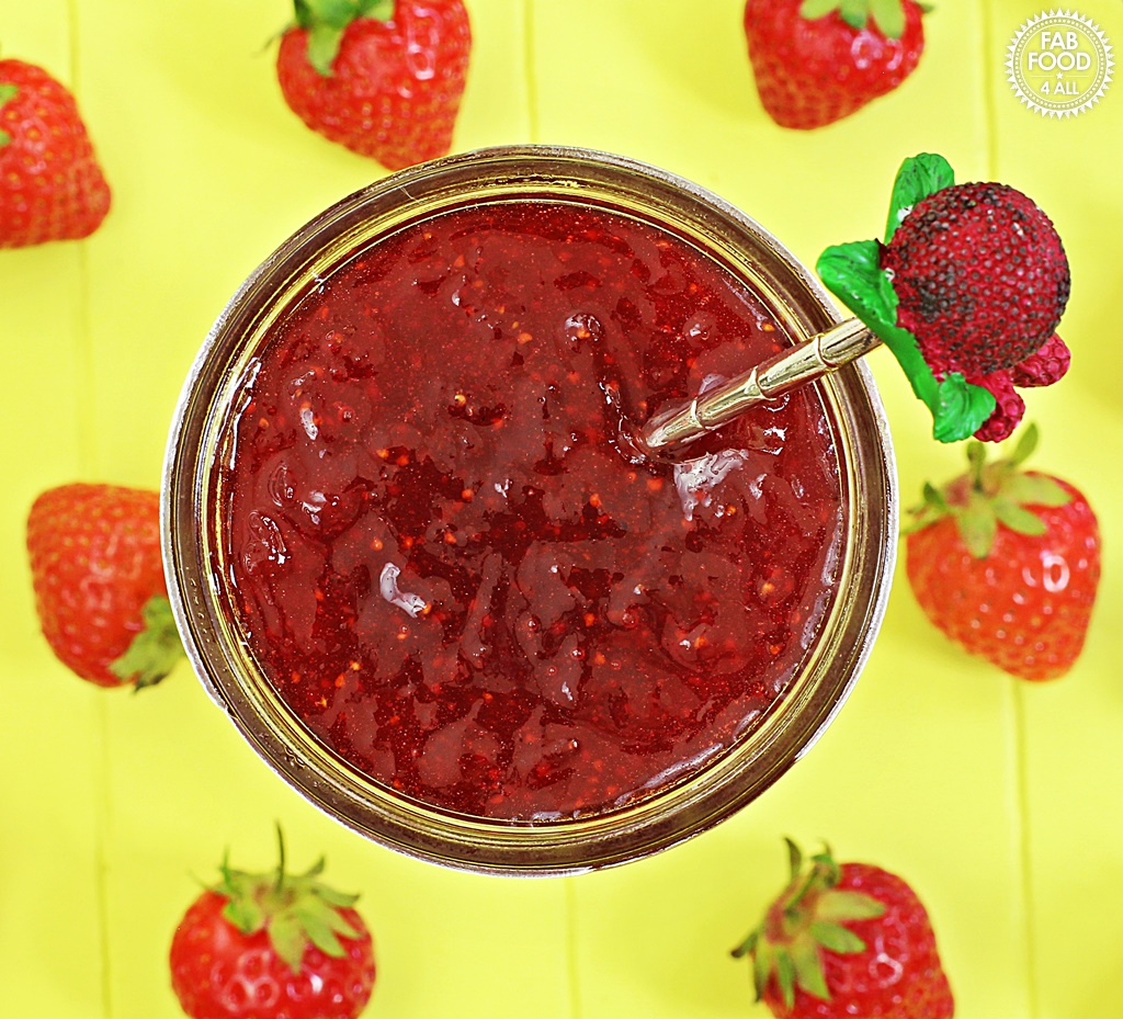 Overhead shot of Quick One Punnet Strawberry Jam in jar with a teaspoon and scattered strawberries.