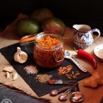 Easy Spicy Mango Chutney with ginger root, garlic, crushed chillies, cardamon, cumin seeds, paprika, salt, red chilli, cider vinegar and soft light brown sugar on a slate.