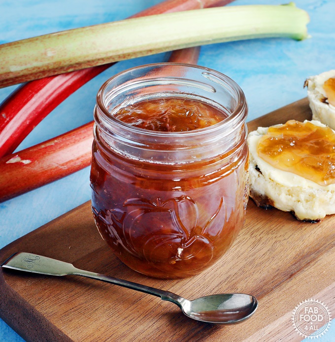 Rhubarb & Ginger Jam on a board with scones flanked by rhubarb stalks.