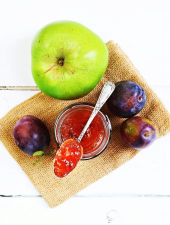 Plum & Apple Jam in open jar with teaspoon flanked by Marjorie plums & a Bramley apple.
