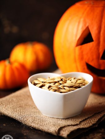 Roasted Pumpkin Seeds in a dish with Pumpkins & jack-o-lantern in the background.