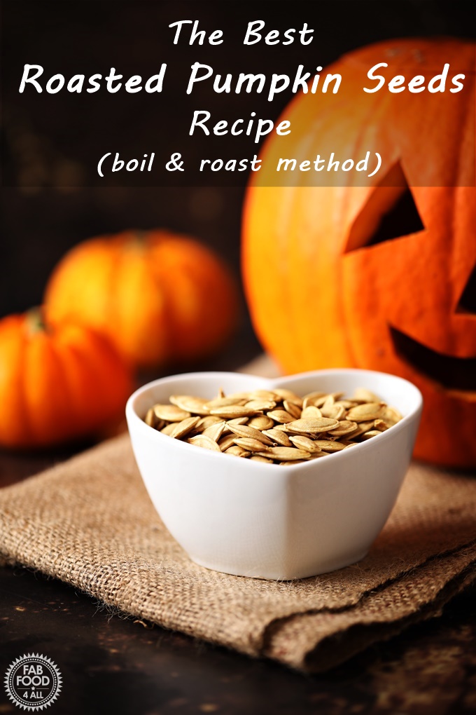 Roasted Pumpkin Seeds in a dish with Pumpkins & jack-o-lantern in the background. Pinterest image.