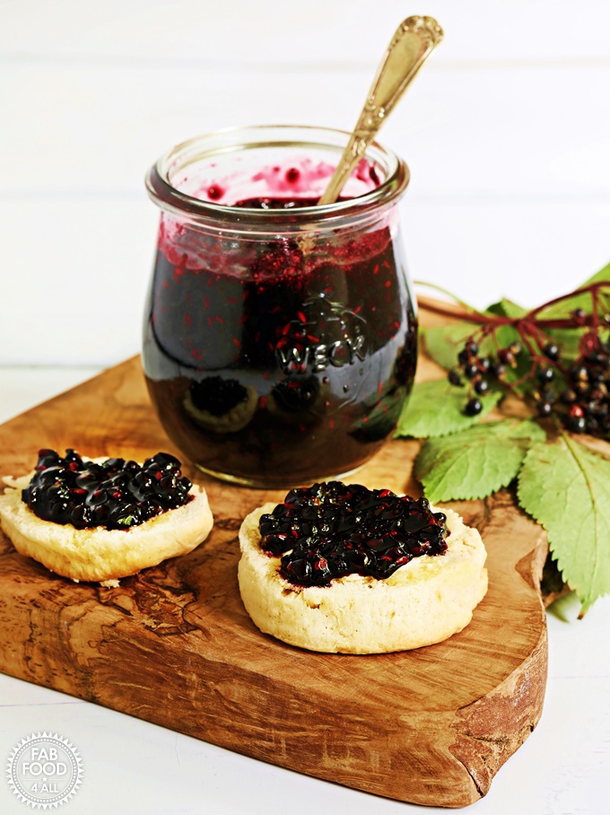 Blueberry Jam in jar with teaspoon submerged on a board with scones.