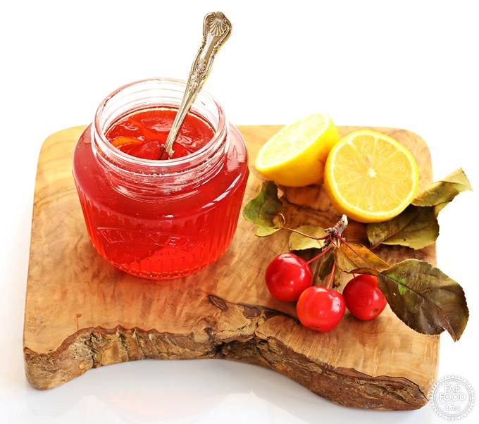 Easy Crab Apple Jelly in a jar with teaspoon on a wooden board with lemon & crab apples.