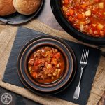 Slow Cooker Beef Stew in a bowl. with rolls & slow cooker.