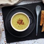 Broccoli & Cheddar Soup in a bowl with spoon & toast on a slate - aerial view.