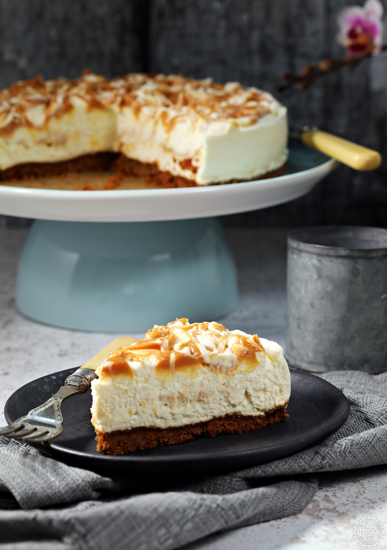 Salted Caramel Cheesecake (no-bake) on a pedestal with cut slice with fork on a plate.