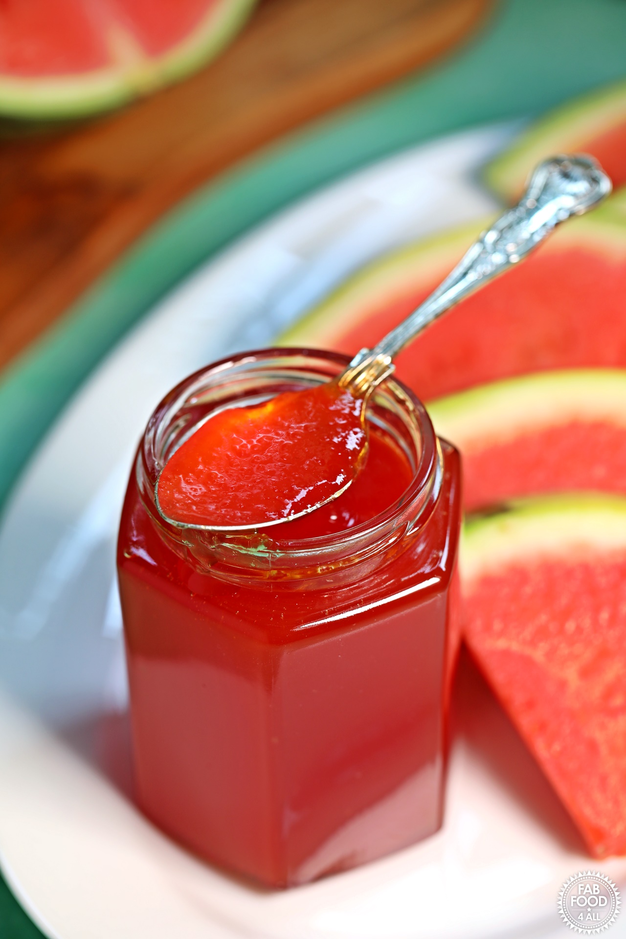 Jar of Watermelon Jam with teaspoon resting on top on a platter with slices of watermelon.