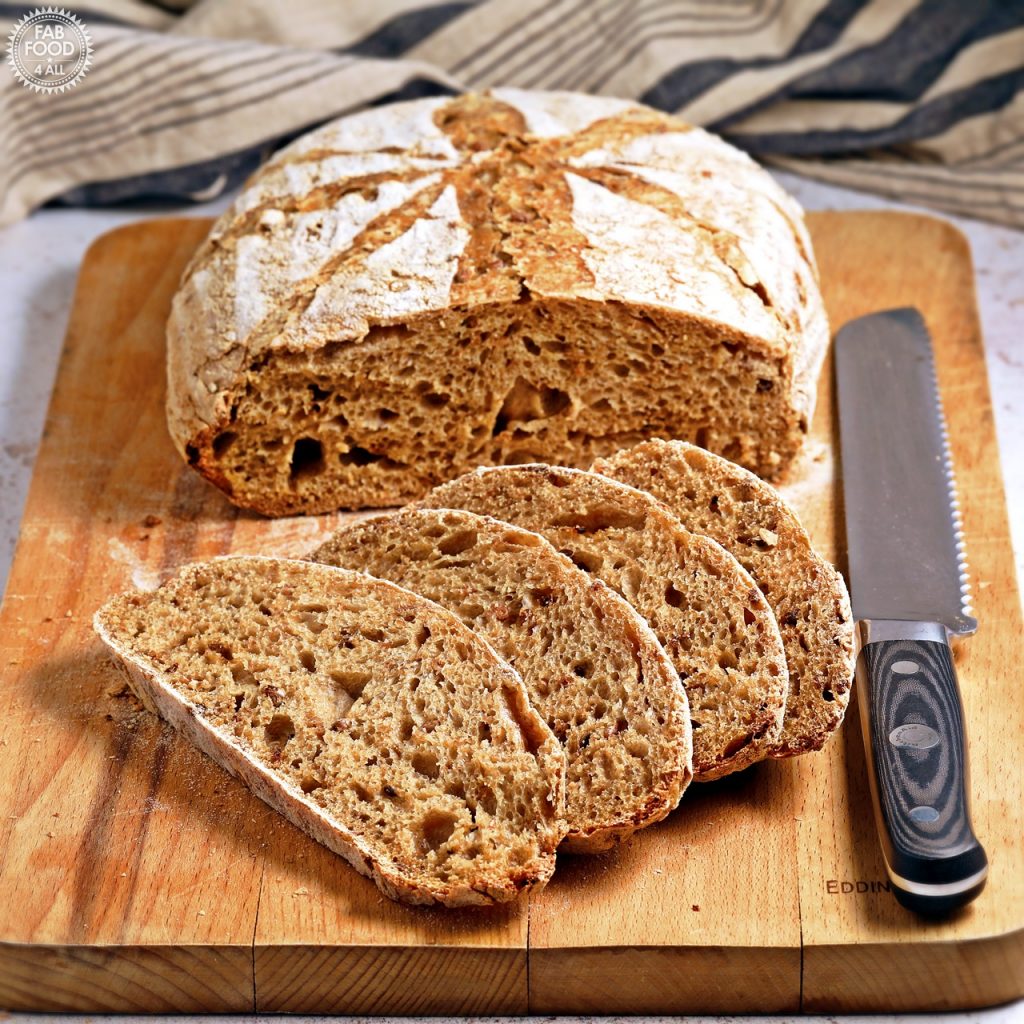 Sliced malted grain sourdough bread on board with knife.