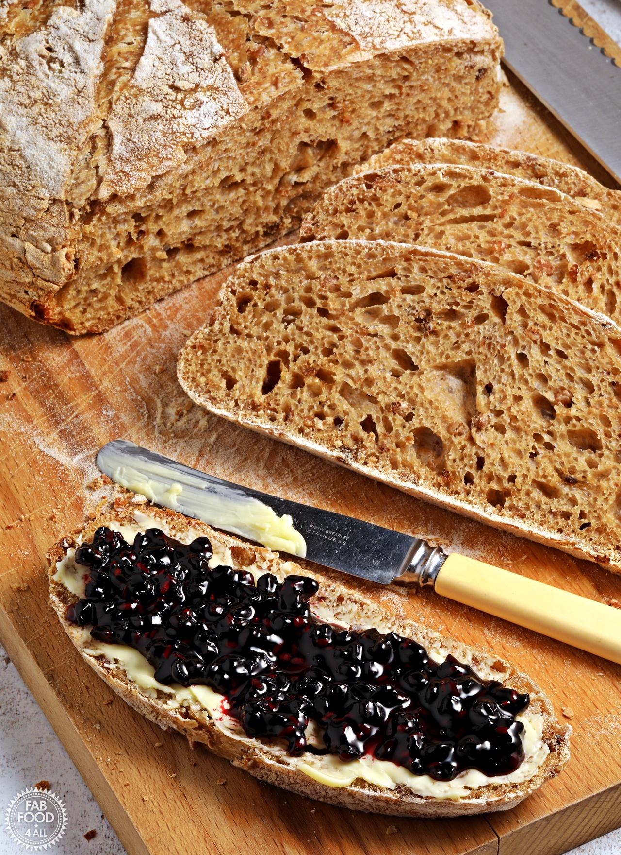 Sliced malted grain sourdough loaf with one slice spread with butter and jam.