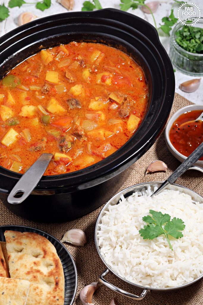 Easy Slow Cooker Beef Curry in slow cooker with bowls of rice, mango chutney & naan bread.