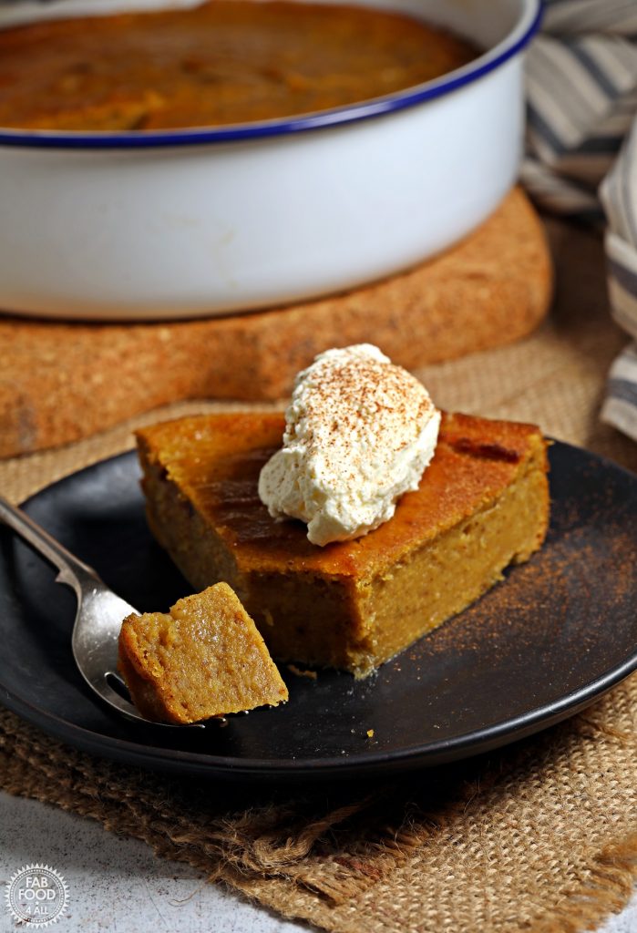 Easy Pumpkin Pie Pudding in pie dish in background and on a plate topped with whipped cream & dusting of cinnamon..