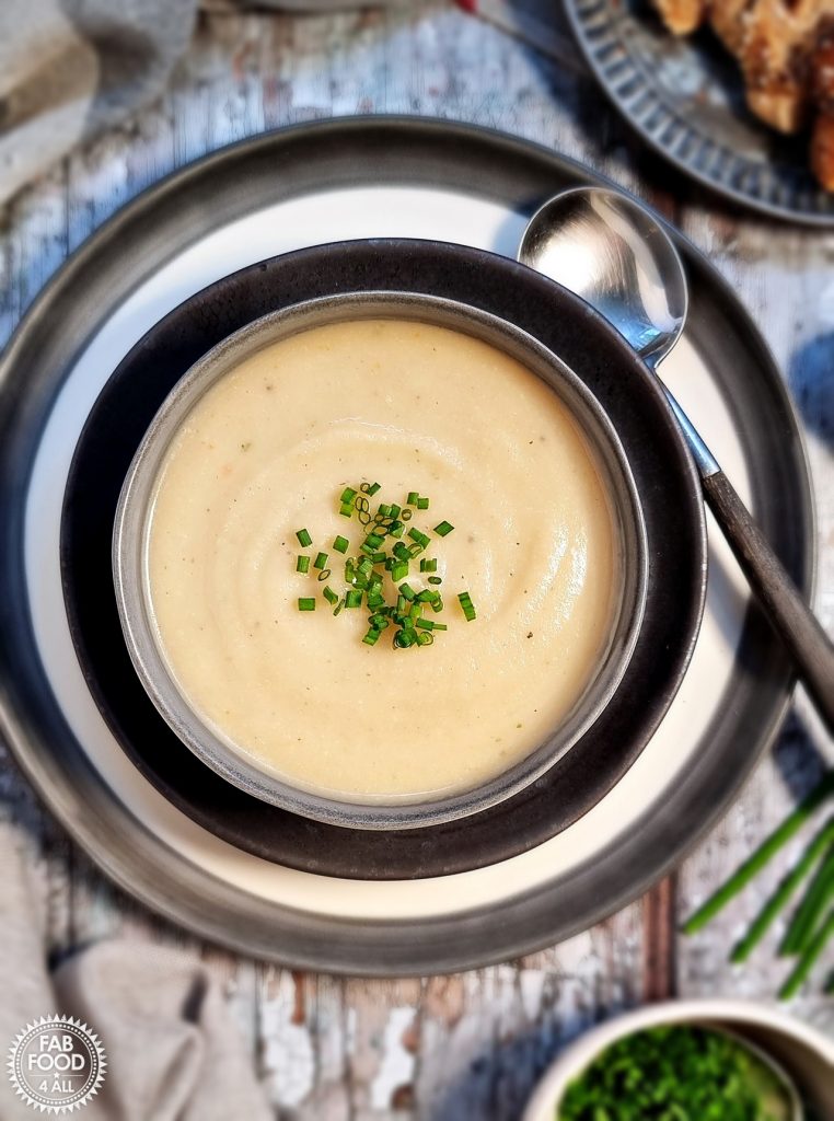 Overhead shot of Easy Roasted Celeriac Soup in a bowl with sliced bread and chive garnish in a bowl.