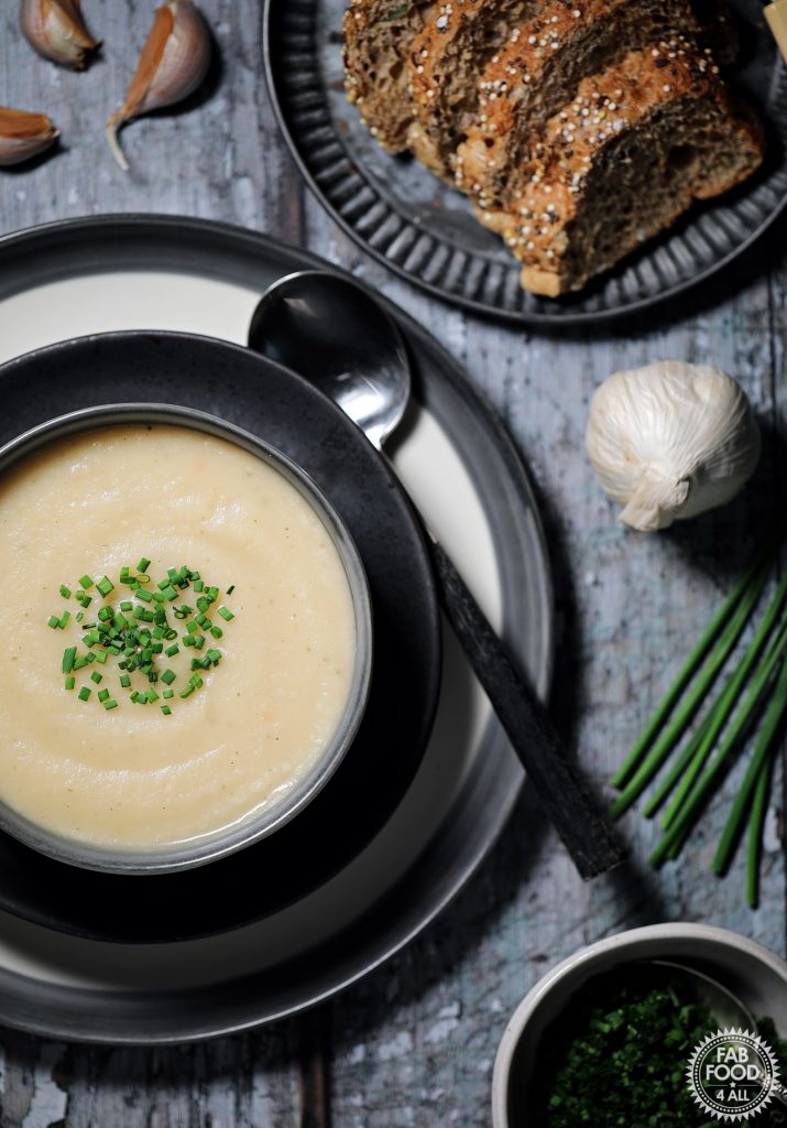 Overhead shot of Easy Roasted Celeriac Soup in a bowl with sliced bread and chive garnish in bowl.