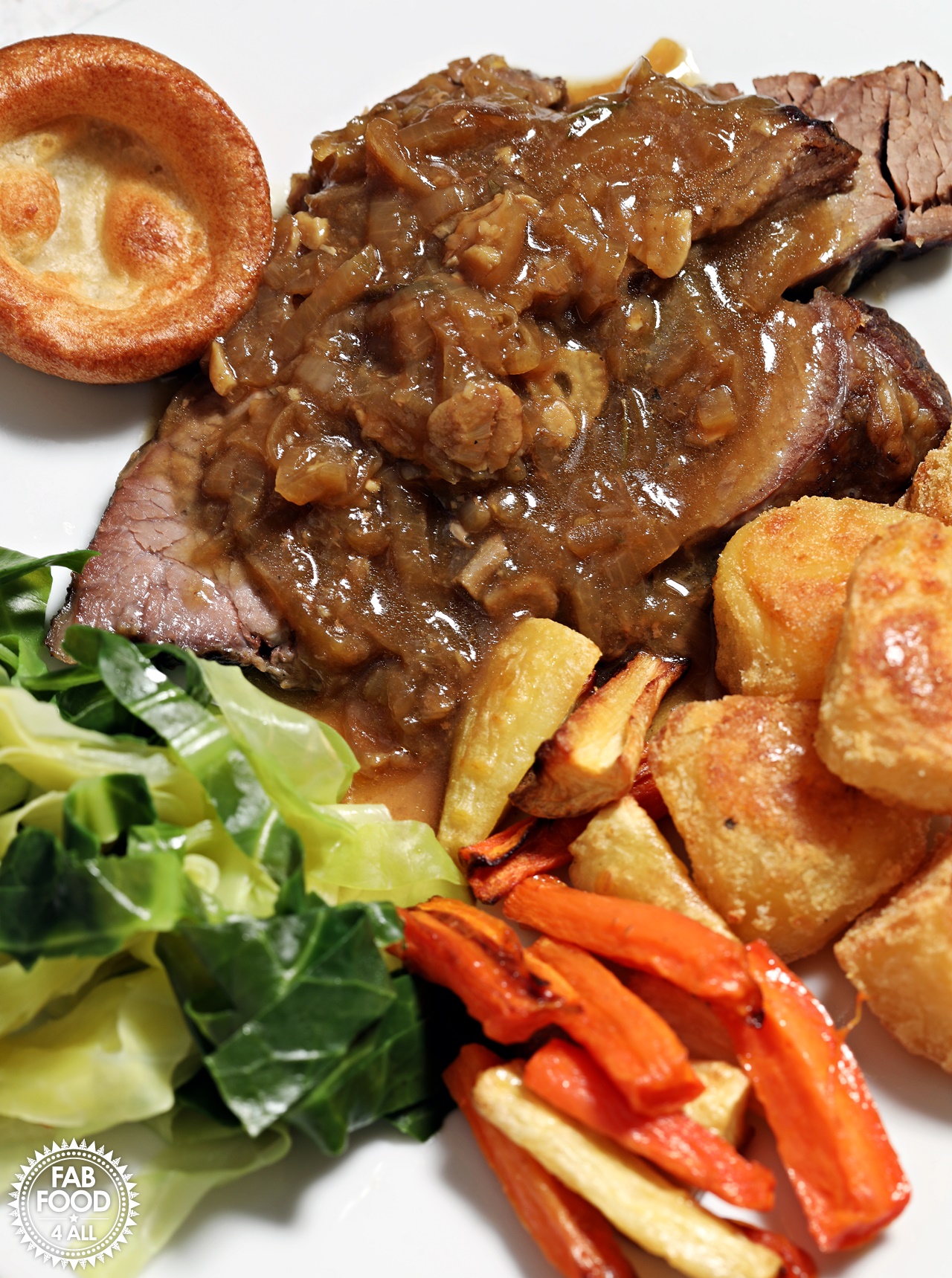 Slow cooked beef brisket with onion gravy, roast potatoes and vegetables on a plate.