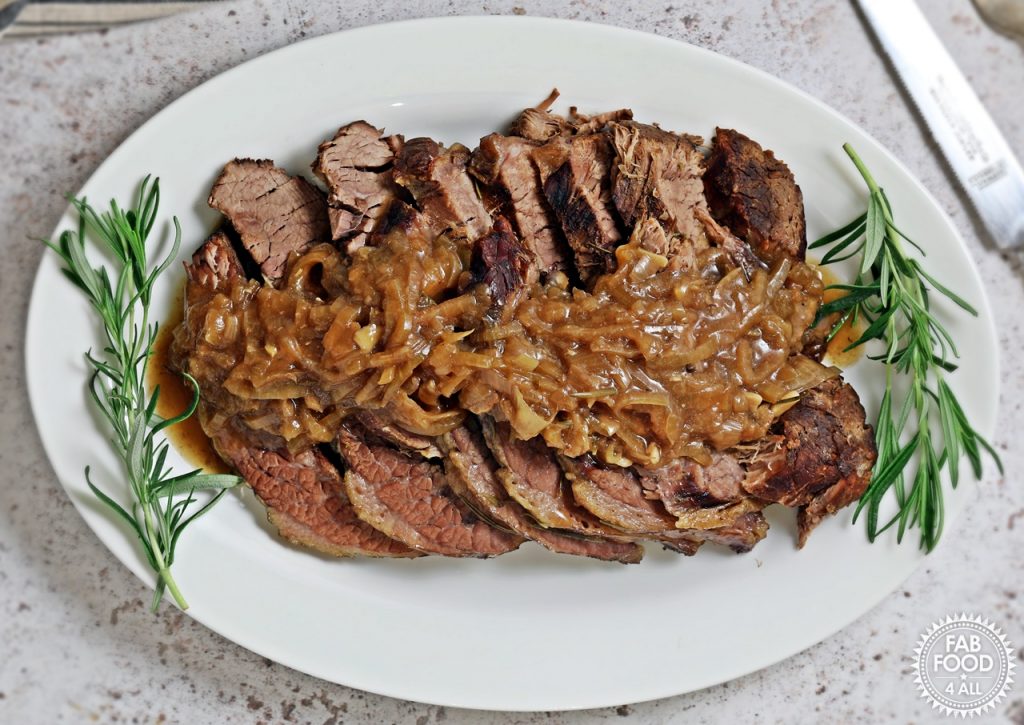 Slow Cooker Beef Brisket with Onion Gravy on a serving platter garnished with rosemary.