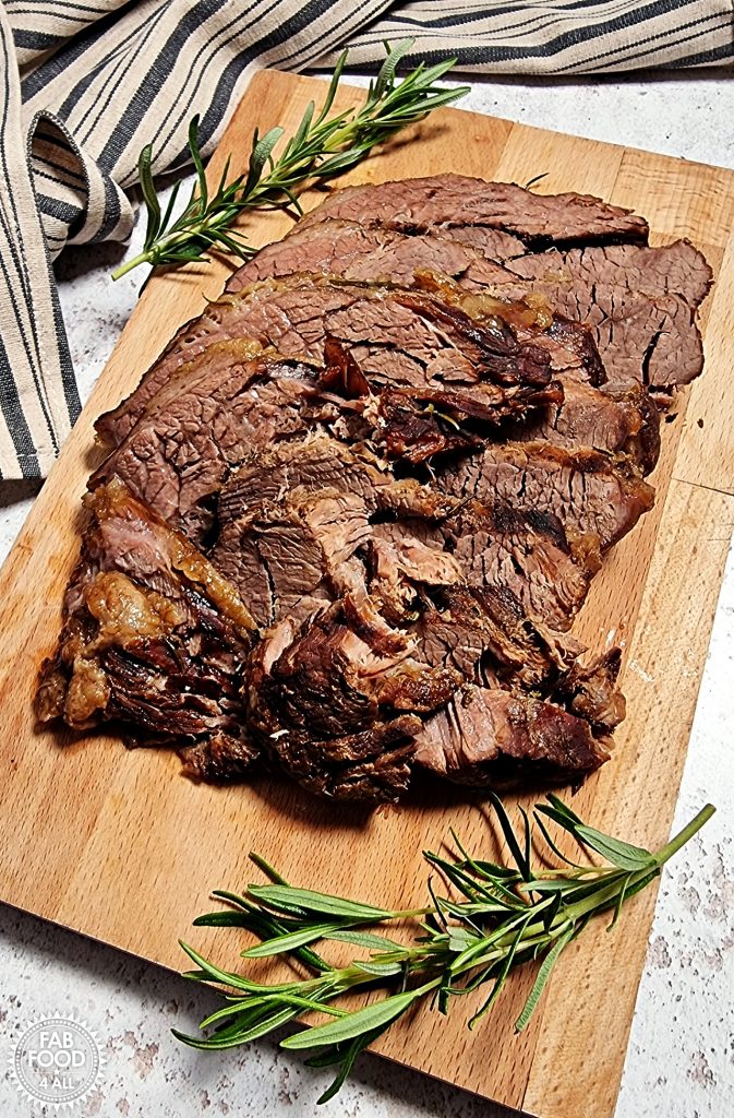 Slow Cooker Beef Brisket carved on a wooden board with sprigs of rosemary.