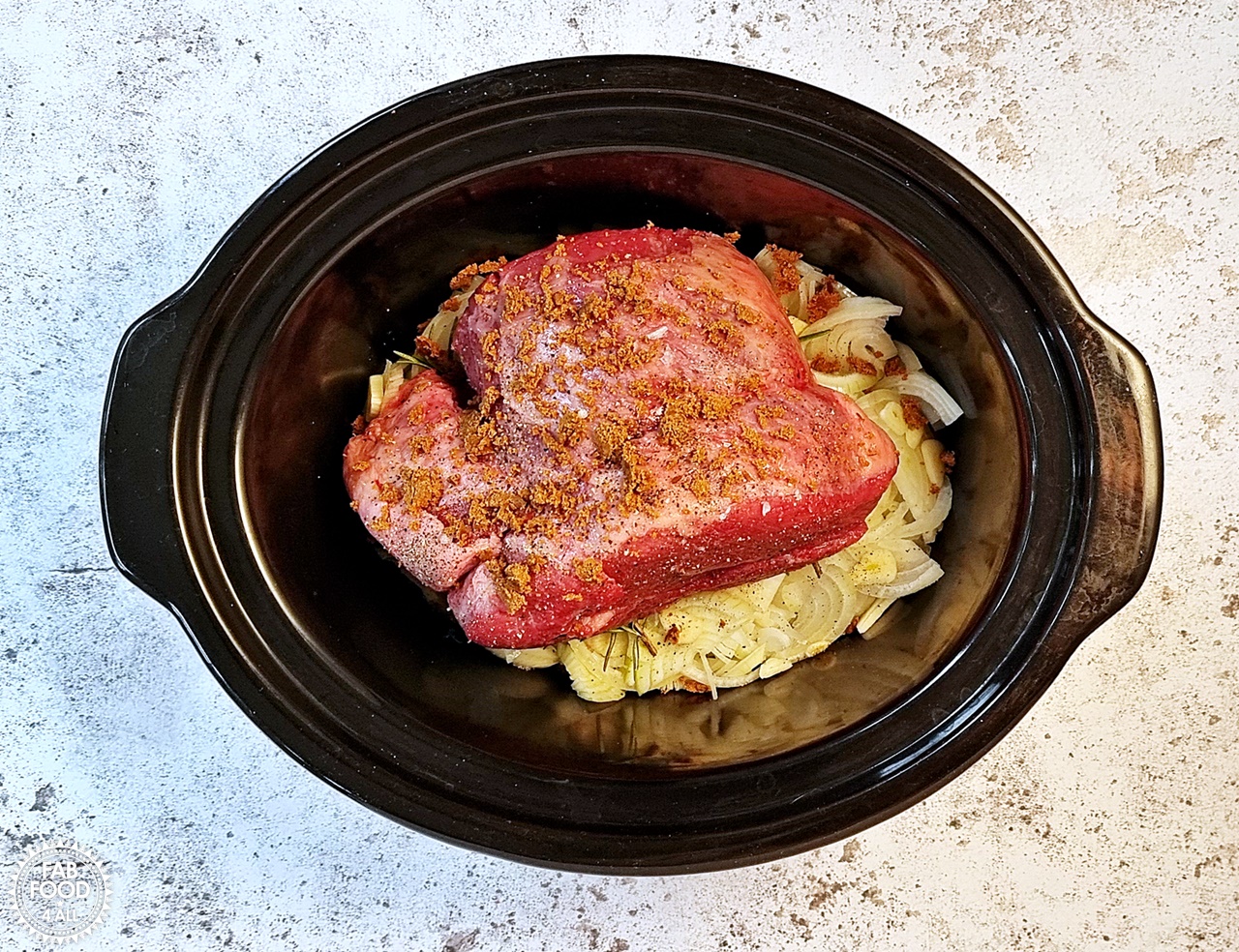 Raw beef brisket joint in slow cooker seasoned with a stock cube, salt & pepper.